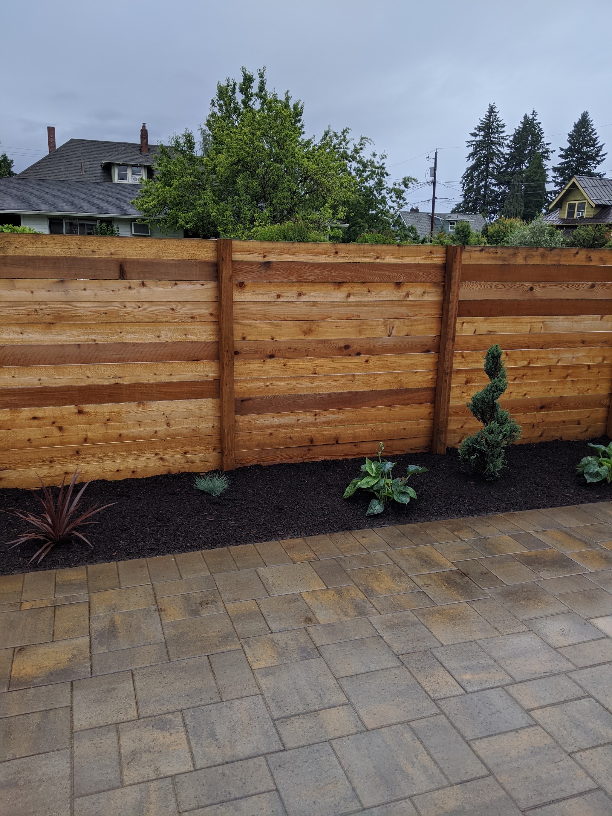 A horizontal cedar fence with a paver patio and a newly planted mulch bed